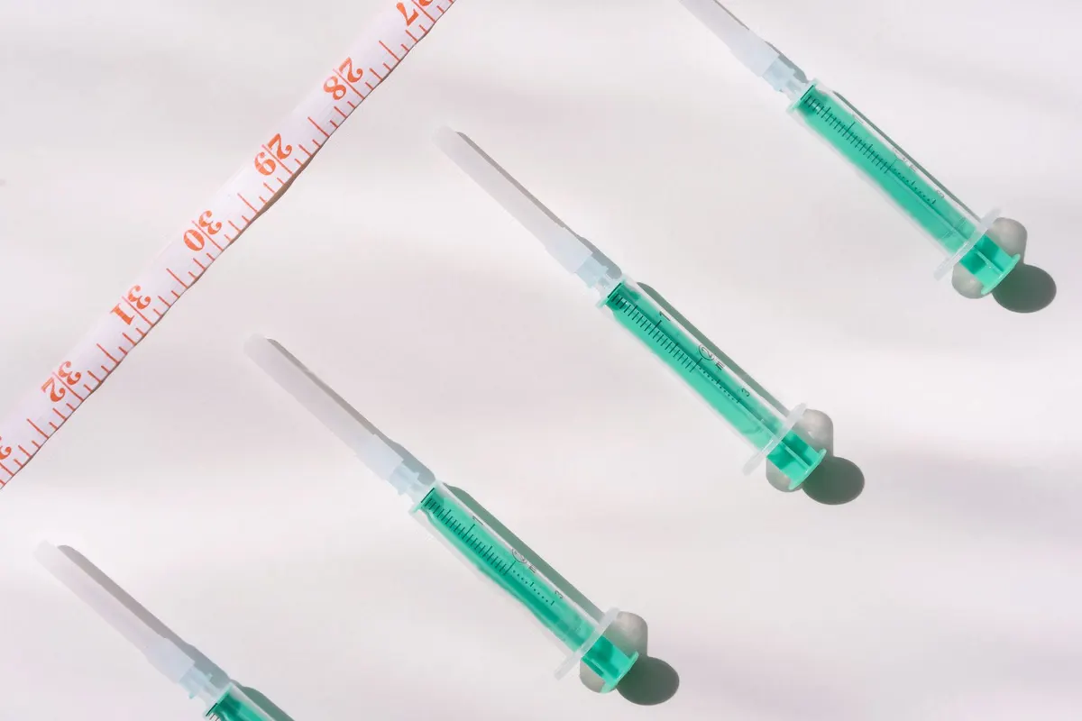 Top view of green filled syringes and measuring tape on a white background, emphasizing healthcare themes.