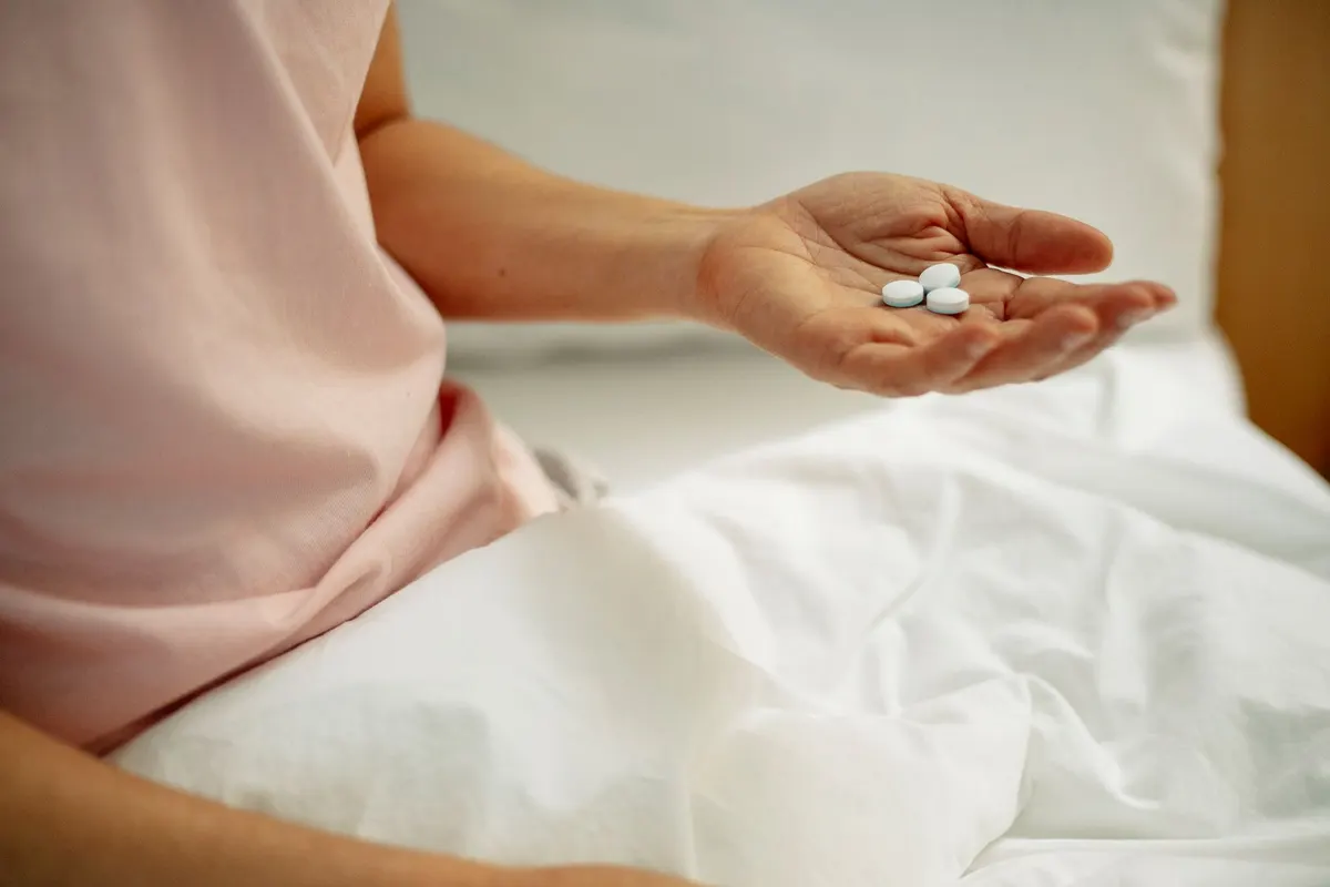 Crop anonymous female with pills in hand in bed with white sheets in hospital