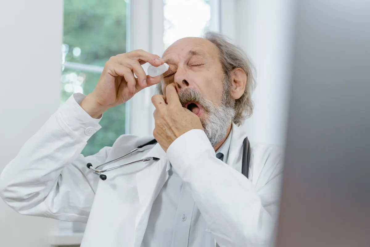 Elderly doctor applying eye drops, emphasizing eye care and senior health.