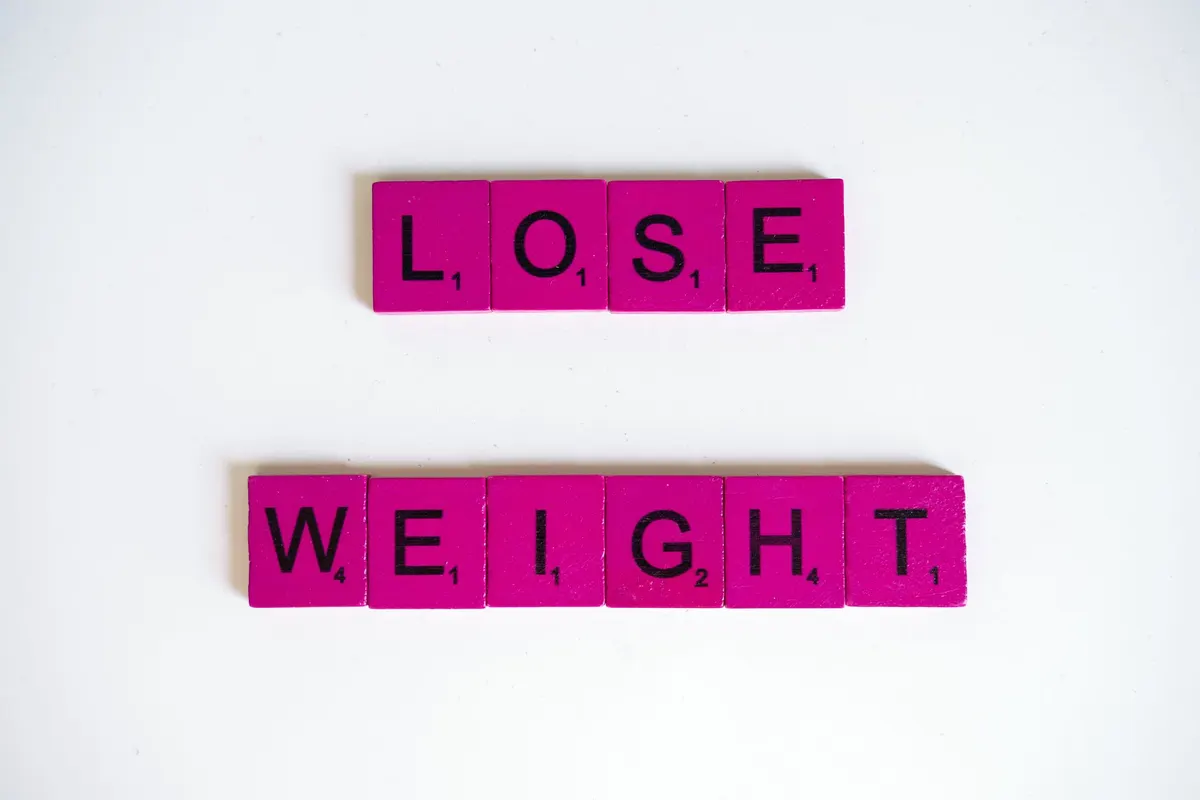 Creative image of the phrase 'Lose Weight' spelled with Scrabble tiles on a white background.