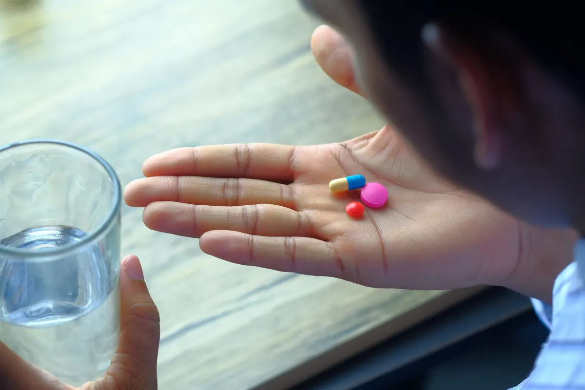 A hand holding a variety of pills alongside a glass of water, emphasizing health and medication.